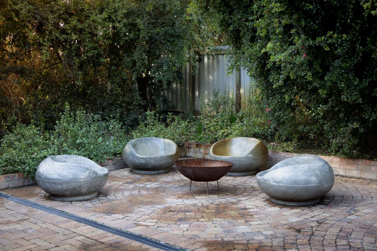 Paver patio with a fire bowl and sculptural stone seats surrounded by greenery